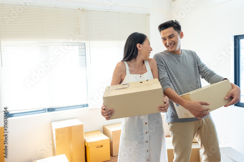 Happy young Asian couple helping and holding moving boxes, looking at each other and smiling