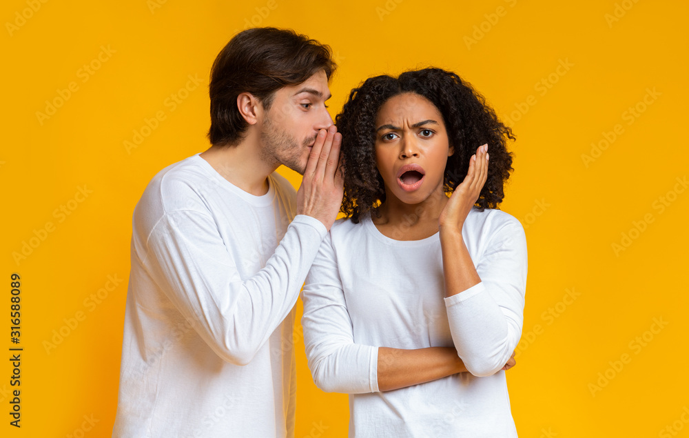Young man gossiping with his girlfriend, whispering secret to her ear Young man gossiping with his girlfriend, whispering secret to her ear