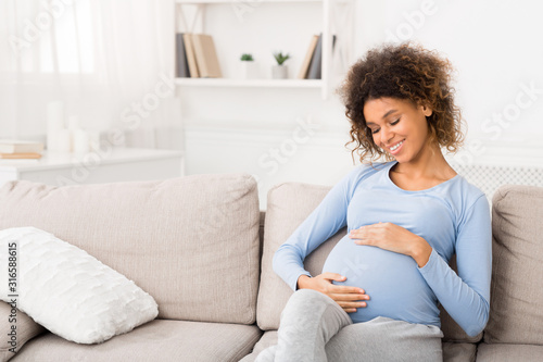 Enjoying pregnancy. Afro girl touching belly and smiling
