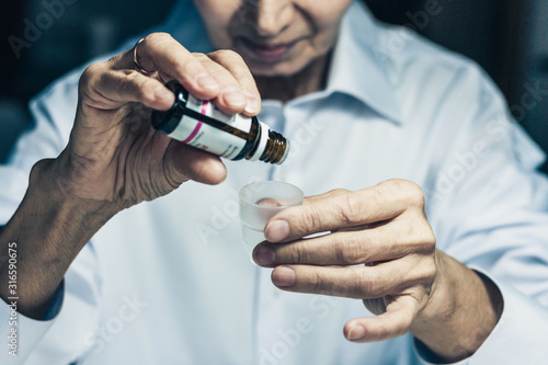 old woman hands close up holding medicine bottle and puts drops in a glass, healthcare concept background with copy space.