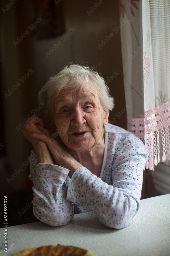 An old russian senior woman is sitting at a table in her house. An old russian senior woman is sitting at a table in her house.