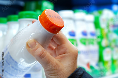 Buyer checks expiration date of dairy product before buying it. Womans hand holding milk bottle in supermarket. Close-up. photo