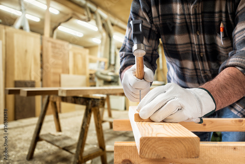 Close-up. Carpenter with his hands protected by gloves with a hammer and nails fixes a wooden board. Construction industry, carpentry workshop.