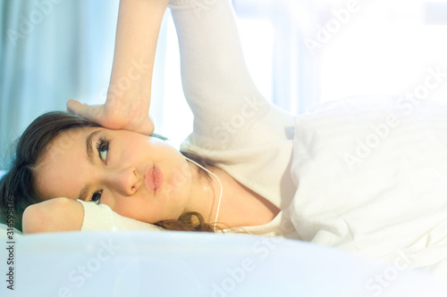 Young girl just wake up in her bed in the morning, listening to music and smiling.