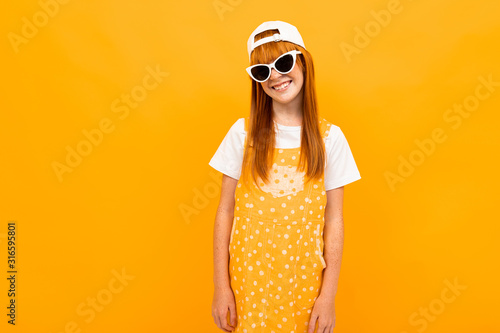 Pretty girl with red hair posing on camera and smiles with sunglasses isolated on yellow background © Ivan Traimak