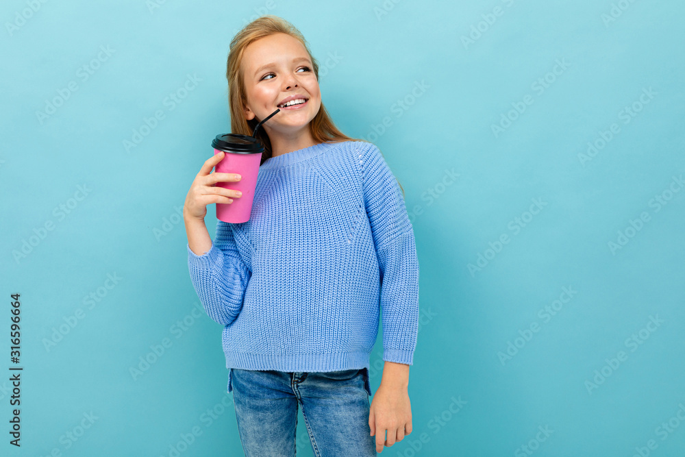 Beautiful caucasian teenager girl with brown hair in blue hoody drinks coffee with pink cup isolated on blue background Beautiful caucasian teenager girl with brown hair in blue hoody drinks coffee with pink cup isolated on blue background