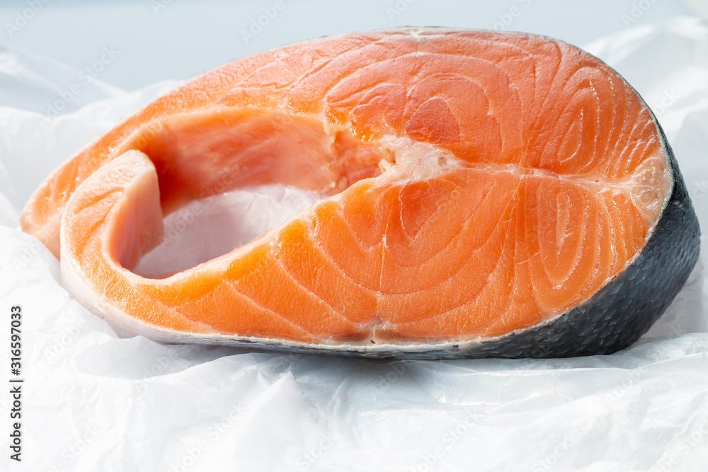 a big piece of raw Atlantic salmon steak on a white creased piece of paper a big piece of raw Atlantic salmon steak on a white creased piece of paper
