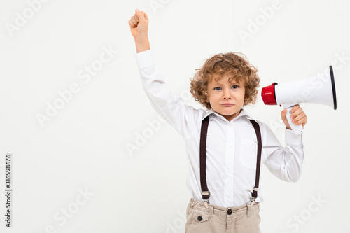 Beautiful boy with curly hair in white shirt, brown hat, glasses with black suspenders listening throung a megaphone isolated on white background photo