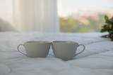 Close up of two white hot cup of coffee on bed in bedroom with copy space in the morning.