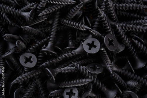 Full frame textured background  - pile of new metal black screws in close-up photo