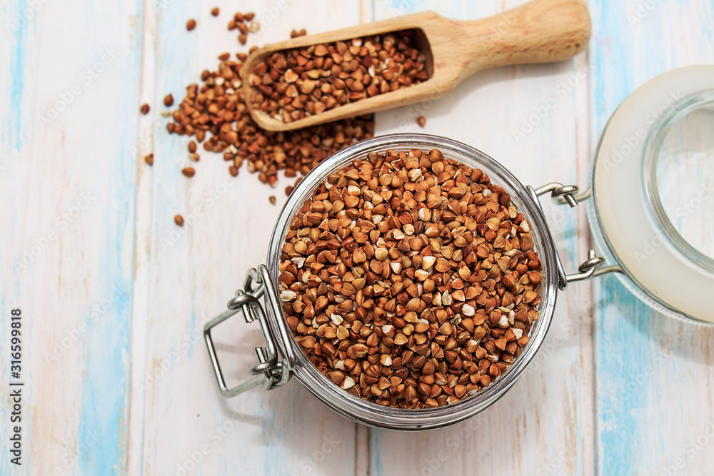 Buckwheat groats in a glass jar on a white wooden background. The concept of healthy nutrition and diet. Buckwheat groats in a glass jar on a white wooden background. The concept of healthy nutrition and diet.