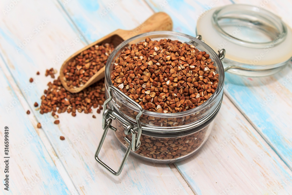 Buckwheat groats in a glass jar on a white wooden background. The concept of healthy nutrition and diet. Buckwheat groats in a glass jar on a white wooden background. The concept of healthy nutrition and diet.