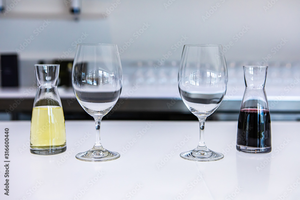 two empty wine glasses and a pair of small decanters filled with white and red wines, taste stemware on a bright white bar counter of the tasting room two empty wine glasses and a pair of small decanters filled with white and red wines, taste stemware on a bright white bar counter of the tasting room