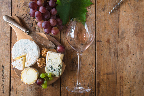 Wine and cheese concept. Various cheeses on cutting board  ripe grapes and glass with the rest of pink wine lying on the old wooden background. Copy space