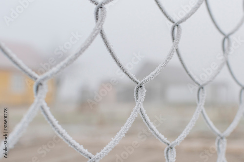 Part of the fence made of metal wire covered with frost