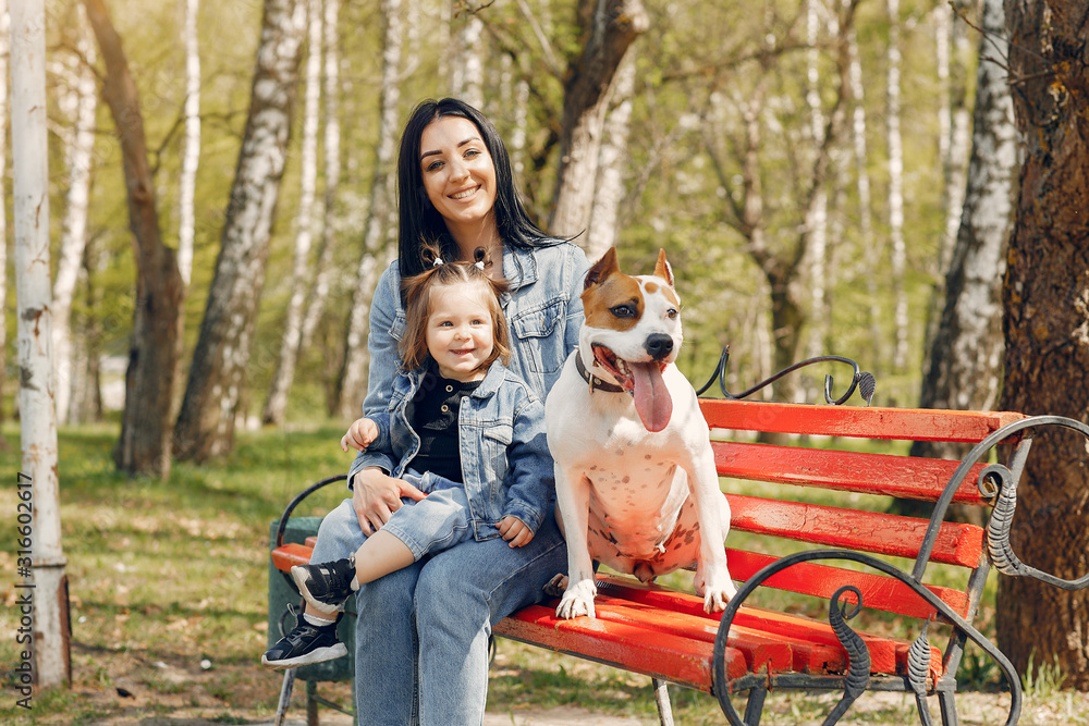 Beautiful mother with daughter. Family in a spring park. Woman in a blue jacket. Family with a cute dog