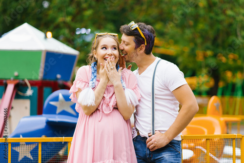Bright cheerful couple in love resting in an amusement Park. The guy whispers in your ear, and the girl is surprised and smiles