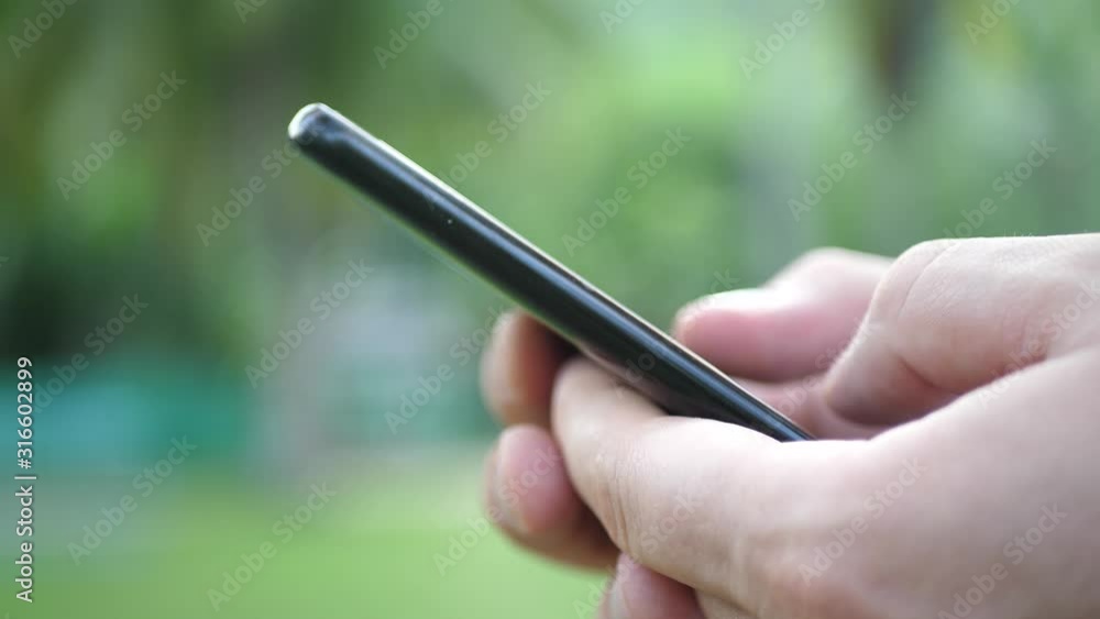 Male Holds Black Phone With Hadns And Plays Game. Background Blurred