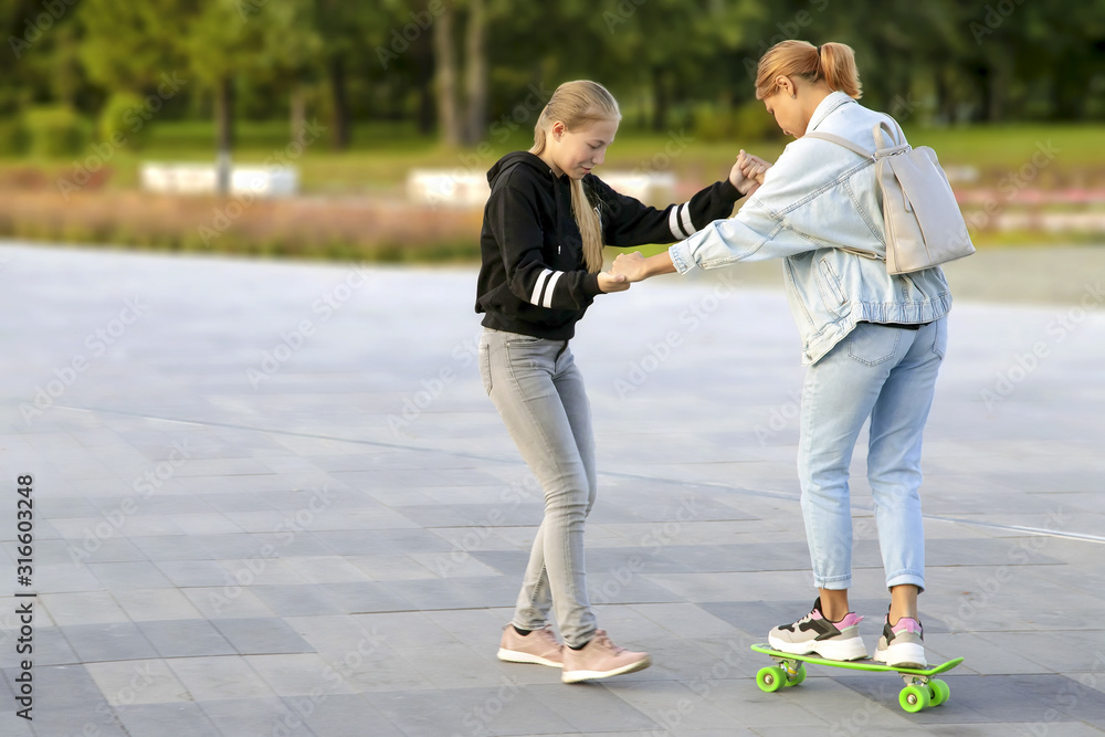 Obraz premium daughter helps her mother ride a skateboard in the city park