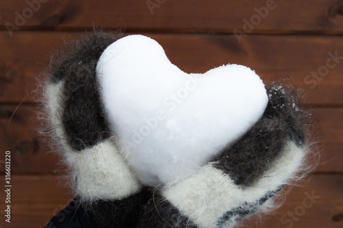 Hands in woolen mittens holding heart shaped snow ball.