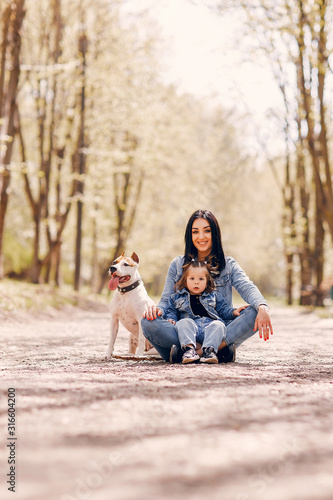 Beautiful mother with daughter. Family in a spring park. Woman in a blue jacket. Family with a cute dog