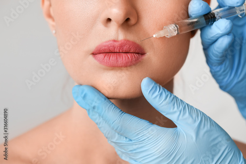 Young woman receiving filler injection against grey background  closeup