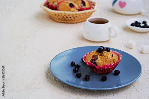 Muffins with black currants on a blue plate on a light concrete background. American cuisine. Copyspace. Selective focus