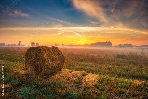 Beautiful summer sunrise over fields with hay bales