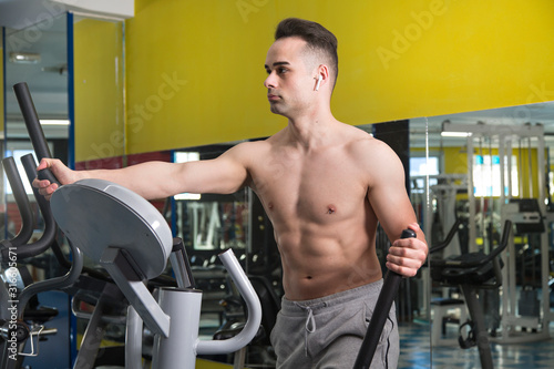 Young muscular man exercising on elliptical machine.