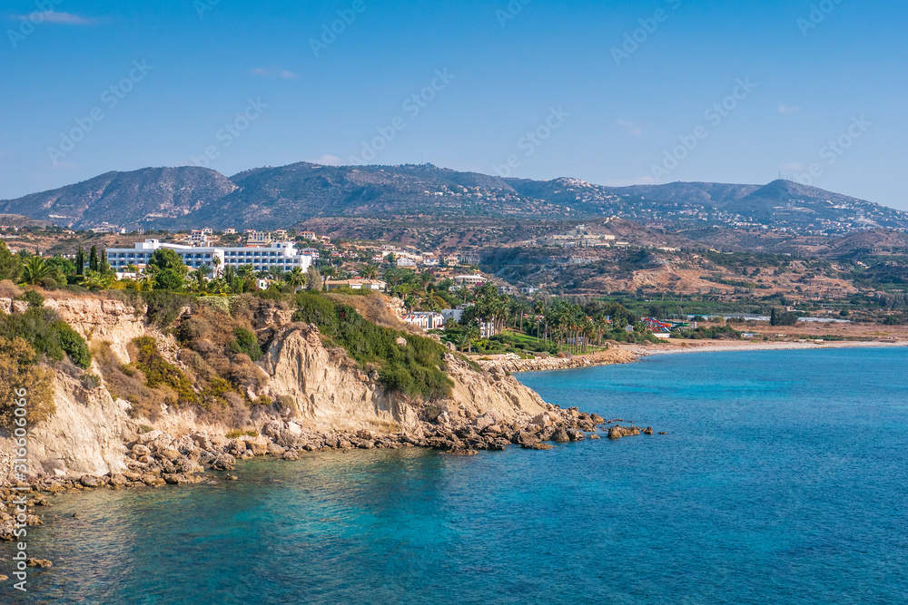 Cyprus landscape. White buildings on stone hill near sea bay with clear transparent water on background of mountains.