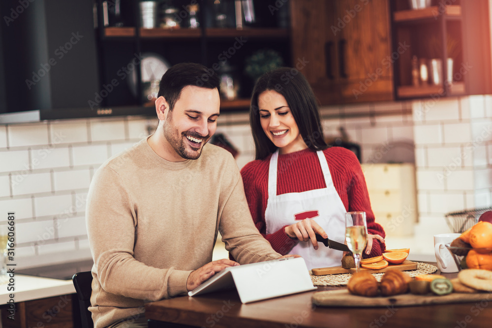 Beautiful young couple is using a digital tablet and smiling while cooking in kitchen at home Beautiful young couple is using a digital tablet and smiling while cooking in kitchen at home