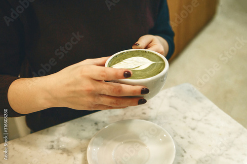 Barista holds a fragrant and healthy matcha latte tea in her hands.