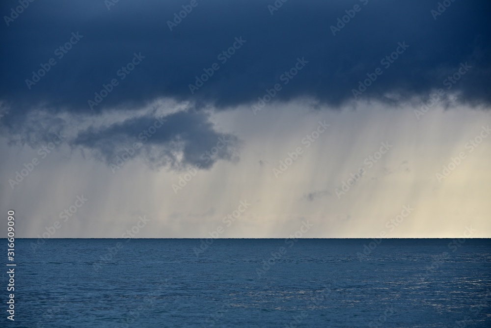 Rainfall over the sea. Heavy clouds float above the water. Abstract sea landscape.