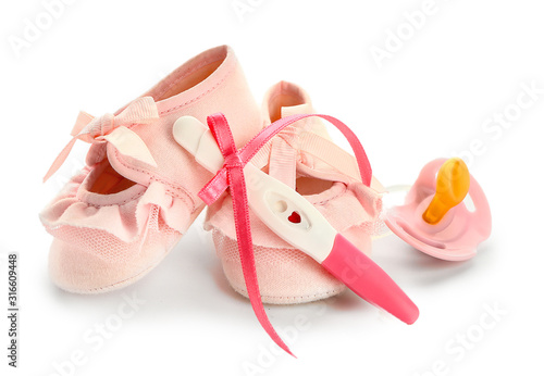 Pregnancy test, baby booties and pacifier on white background