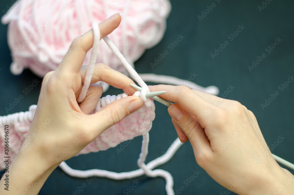 A young girl knits something with pink threads, black background