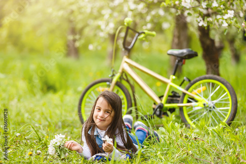 little girl with bike near flowering trees in spring