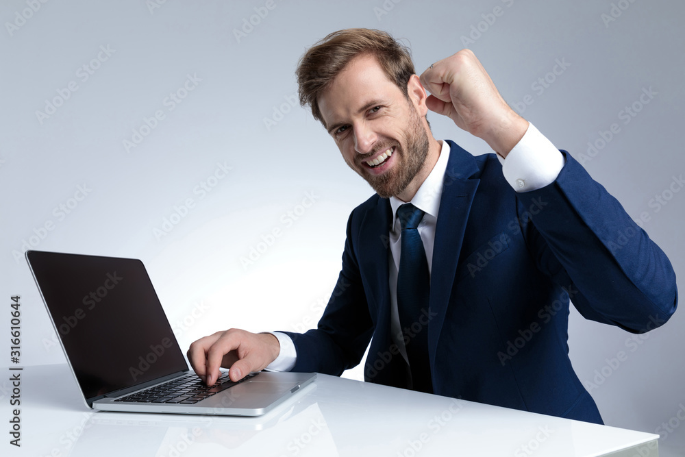 Positive businessman celebrating and writing on his laptop