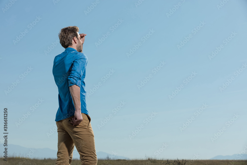 casual man standing with hand in pocket and protecting eyes casual man standing with hand in pocket and protecting eyes