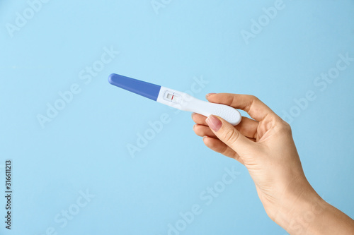 Female hand with pregnancy test on color background