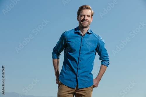 casual man standing with hands behind him happy