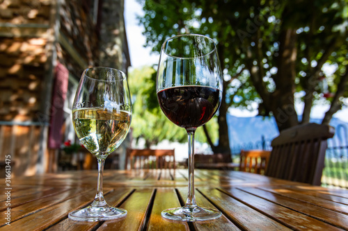 pair of different glass sizes and wines  red and white wine glasses on wooden furniture table close up selective focus  vineyard farmhouse patio view