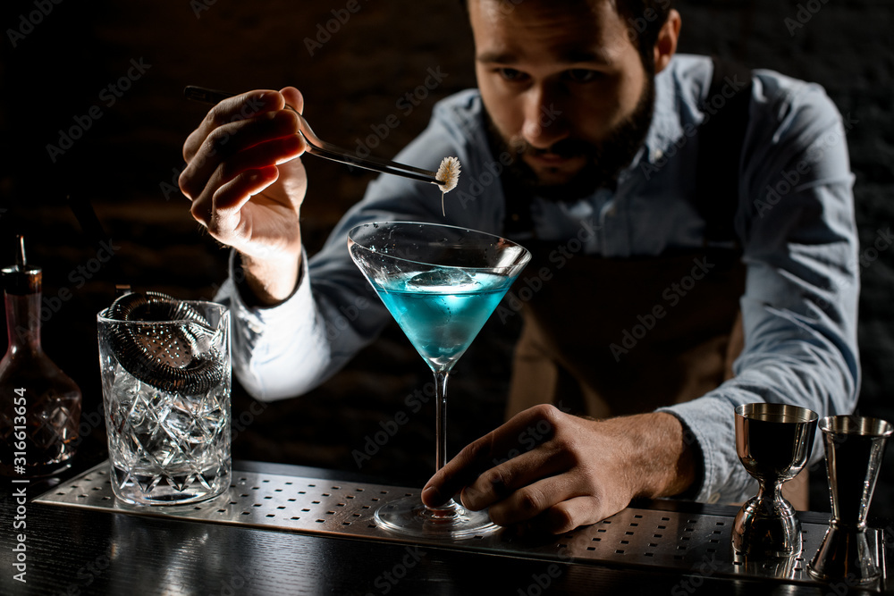 Professional bartender deacorating a blue alcoholic cocktail in a martini glass with a spikelet