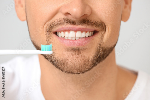 Handsome man with tooth brush on grey background, closeup