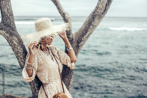 Boho model wearing dress and straw hat on the beach