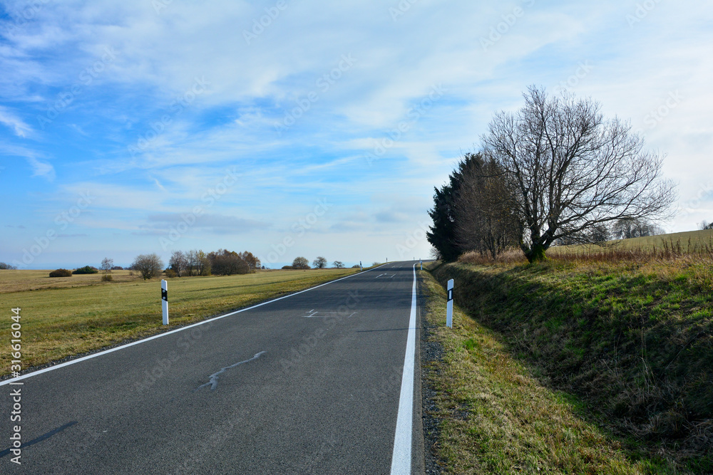 Lonely road through a green landscape, with blue sky in the Rhoen, Bavaria, Germany Lonely road through a green landscape, with blue sky in the Rhoen, Bavaria, Germany