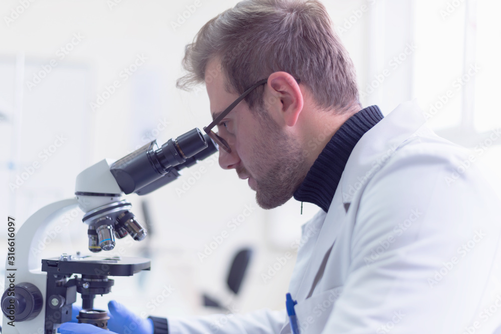 Young male scientist looking through a microscope in a laboratory doing research, microbiological analysis, medicine. Young male scientist looking through a microscope in a laboratory doing research, microbiological analysis, medicine.