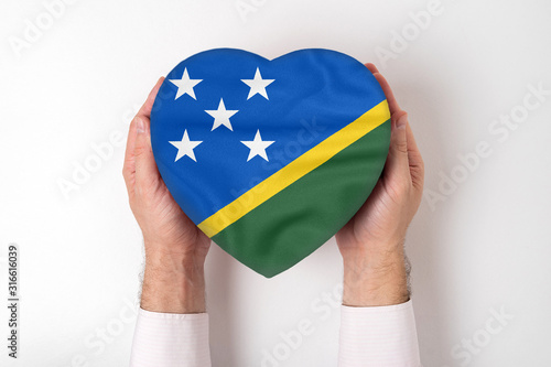 Flag of Solomon Islands on a heart shaped box in a male hands. White background