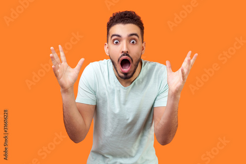 Obraz na plátně Oh my god, wow! Portrait of amazed brunette man with beard in white t-shirt staring at camera with big eyes and open mouth, absolutely shocked by news
