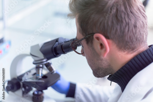 Young male scientist looking through a microscope in a laboratory doing research, microbiological analysis, medicine.