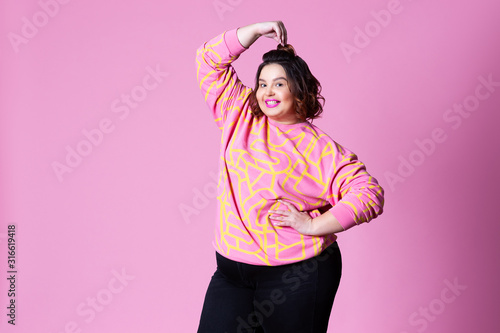 Happy plus size model in casual clothes, fat woman on pink background photo